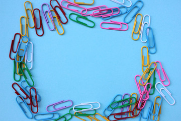 Top view of colorful paper clips on blue background with copy space. Back to school or office concept
