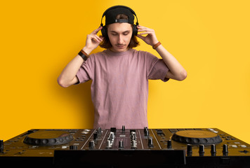 dj man in white headphones behind dj console, makes song with dj controller. long haired caucasian guy in cool stylish wear posing on isolated background - obrazy, fototapety, plakaty