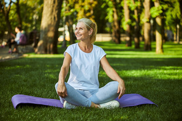 Cheerful woman sitting on yoga mat outdoors