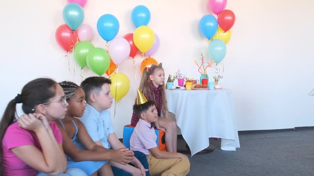 animator shows magic trick with empty cardboard box to happy little children in decorated room at birthday party slow motion