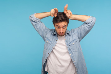 Portrait of aggressive man in worker denim shirt standing with bull horn gesture and looking...