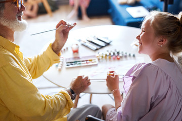 cute little girl and senior granddad painting with colorful paints at home, they spend time...
