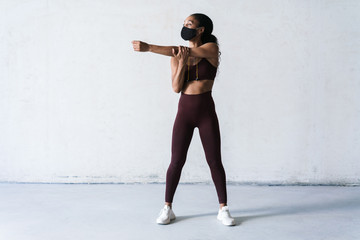 Photo of athletic african american woman in face mask doing exercise - Powered by Adobe