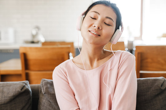 Smiling asian woman on couch listening to music at home