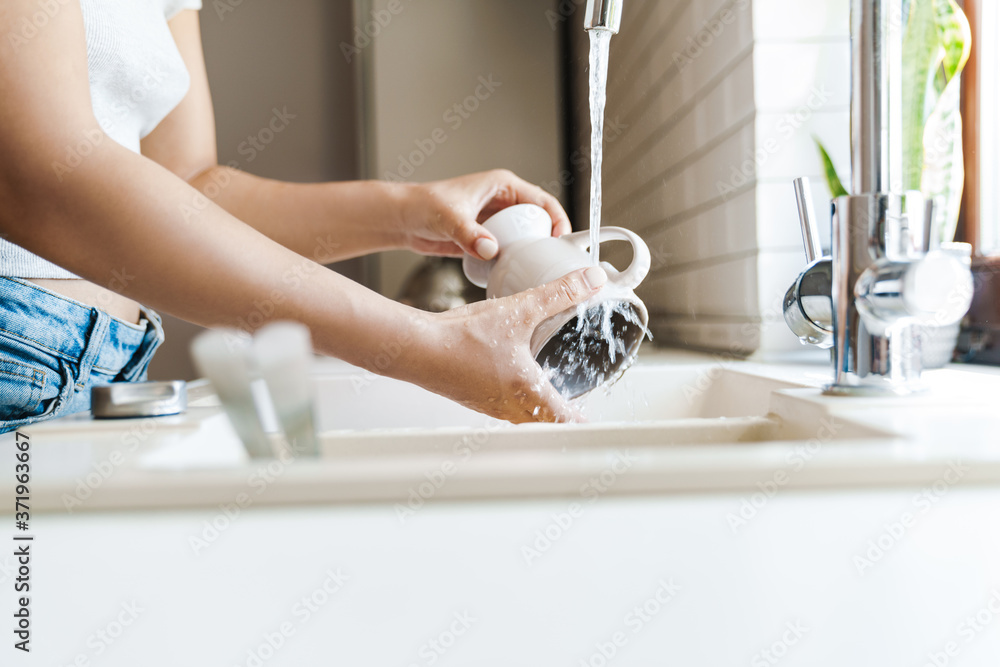 Wall mural Beautiful young woman washing dishes at the sink