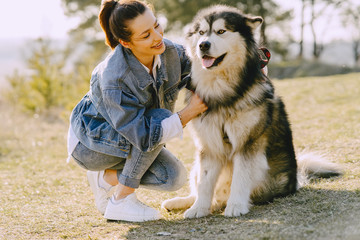 Woman in a spring forest. Girl with cute dog. Brunette in a jeans jacket.