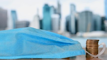 Blue Surgical Mask falls on the stack of coins. Impact of COVID-19 Pandemic on Economy. Concept Video. - Powered by Adobe
