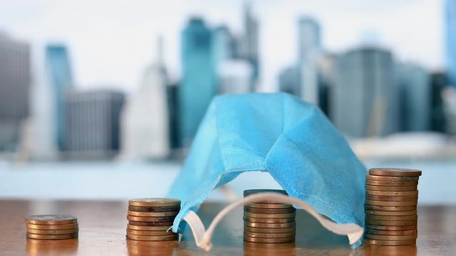 Economic Impact of Coronavirus Pademic. Blue Surgical Mask falls on the stack of coins. Impact of COVID-19 Pandemic on Economy.