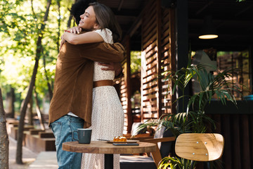 Image of happy young multinational couple hugging in cafe outdoors