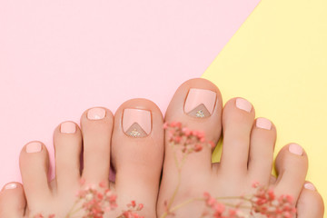Female feet with cream nail design. Pink nail polish pedicure on pink yellow background.