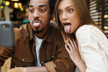 Image of couple showing her tongues and taking selfie on cellphone