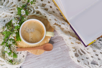 Cozy home still life: cup of hot coffee, spring flowers and opened book with warm plaid. Springtime concept, free copy space. magic bokeh background. morning affirmations concept