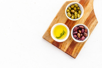 Green and black olives, olive oil in bowls on cutting board top-down copy space