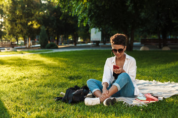 Obraz premium Woman sitting on grass in park while using smartphone