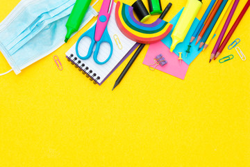 Back to school concept. Face mask, colorful pencils, rainbow eraser, notebook, sticky notes and office supplies. Flat lay. Abstract educational background.