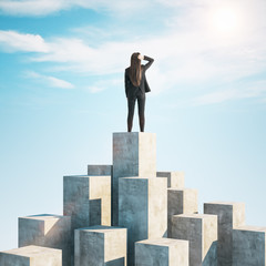 Businesswoman standing on concrete cube and look into distance.