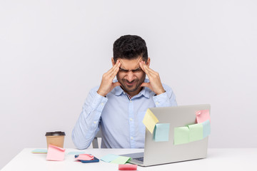 Migraine of stressful job. Depressed man employee sitting in office, clasping head temples,...