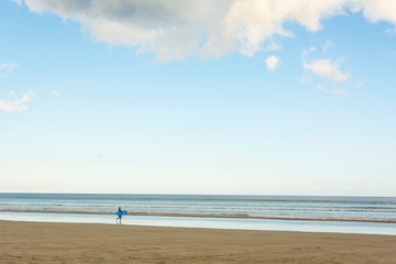 Child surfer entering the water with the surfboard on a cloudy day