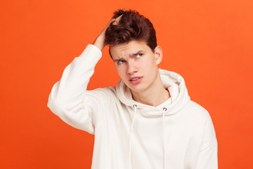 Thoughtful young man in casual hoodie holding his hand on head with puzzled face,problems with concentration, forget about important event. Indoor studio shot isolated on orange background - obrazy, fototapety, plakaty