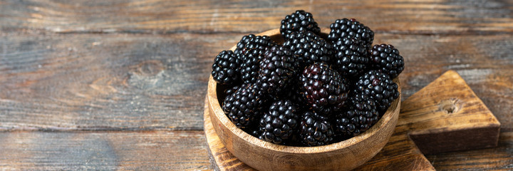 Blackberries in a wooden bowl on a brown wooden table. Fresh blackberries in a bowl close-up. Space for text. Banner	