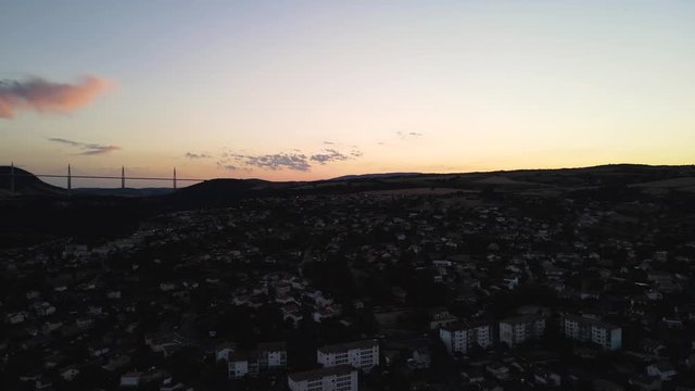 Aerial panoramic view of beautiful french city of Millau, France and famous Millau viaduct after sunset. Romantic french city nested among the hills in the evening golden hour light.