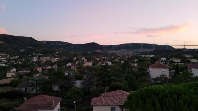 Evening golden hour aerial view o small historic town of Millau, France. Drone overflying scenic french city flying toward Millau viaduct nested between the hills.