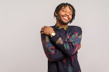 Satisfied pleased african man in casual sweatshirt with dreadlocks hugging himself, egoistically...