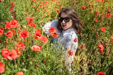 Young woman is standing near blooming poppy field