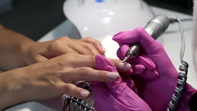 Close-up of manicurist removes gel shellac polish from client's nails using manicure machine.
