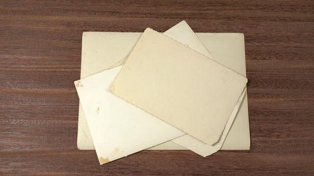 Stack of old vintage paper photos stacked together on brown wooden table surface background. Back view of old snapshots.