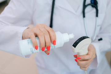 Close-up of female doctor applying the ultrasound gel to the scanner for performing ultrasound of belly of pregnant woman in medical clinic. Concept of happy and healthy childbearing.