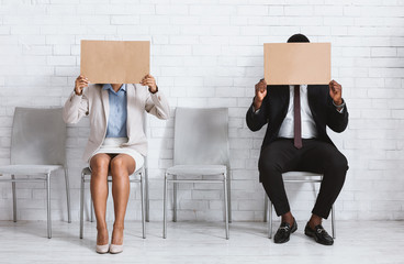 African American job applicants closing their faces with blank signs at company office, space for...