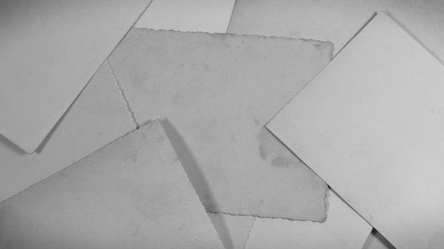Stack of old vintage paper photos appear stacked together on wooden table surface background. Back view of photo pictures. Black and white video background.