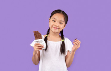 Chinese Girl Eating Chocolate Posing Over Purple Background In Studio