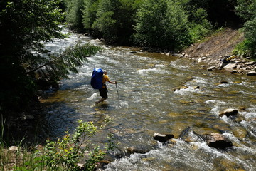 Fototapeta premium Hiker man hiking crossing river. Trekking journey and travel concept
