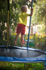 Happy child, active boy plays outdoors in playground jumping high on trampoline.