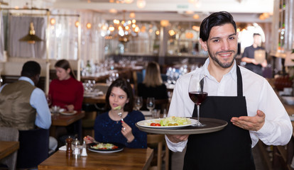 Portrait of smiling waiter with serving tray meeting restaurant guests