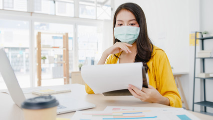 Asia businesswoman entrepreneur wearing medical face mask for social distancing in new normal situation for virus prevention while using laptop back at work in office. Lifestyle after corona virus.