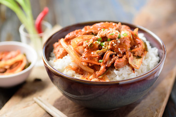 Stir fried kimchi with pork on cooked rice in a bowl on wooden background, Korean food