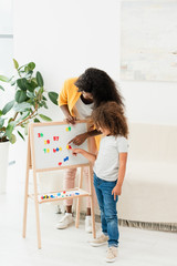 african american mother and daughter pointing with fingers at magnets on whiteboard