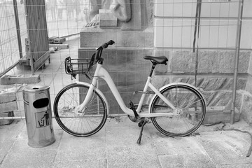 Fototapeta na wymiar Mülleimer und Fahrrad für Damen am Gitter vor einer Baustelle in der Hauptstadt Berlin, fotografiert in klassischem Schwarzweiß