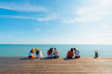 Photos from the back of Asian women wearing colorful colored clothes sitting on the balcony by the sea. They tilted their heads together in pairs. Feelings of love, friendship, and happiness.