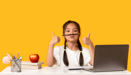 Funny Asian School Girl At Laptop Gesturing Thumbs-Up, Yellow Background