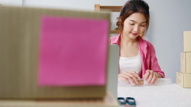 Young Asia entrepreneur businesswoman packing product in cardboard box deliver to customer, working at home office. Small business owner, start up online market delivery, lifestyle freelance concept.