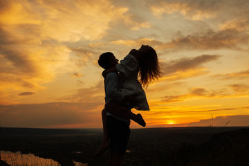 Young couple hugging on amazing orange sunset on the mountain. Enjoyment, playful, dancing,  summer vacation, sunny.