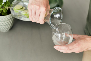 Person, die sich Wasser/Hausgemachte Limonade aus einer Karaffe in ein Glas schüttet