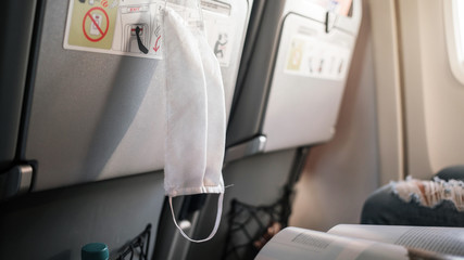 white protective medical facemask hanging on back of airplane seat during travel flight