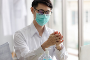 Young Asian businessman wearing a maskand washes his hands with an alcohol gel inside a working office.  New normal way of life during the epidemic and after the COVID-19 epidemic.