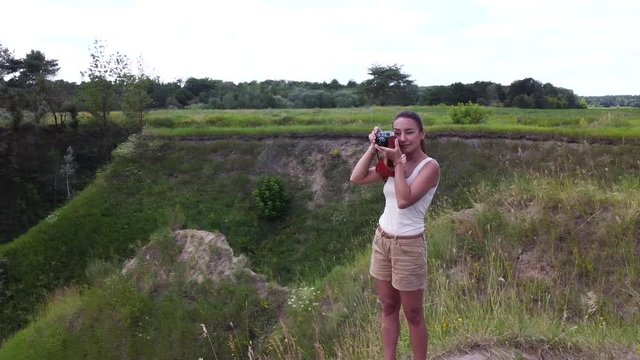 Single young girl tourist takes pictures by old film camera standing on the top of the hill