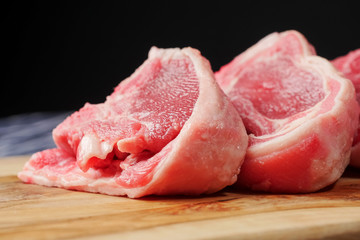 Stack of fresh raw lamb loin chops on a wooden board and white and blue table cloth, black background. Meat industry concept.
